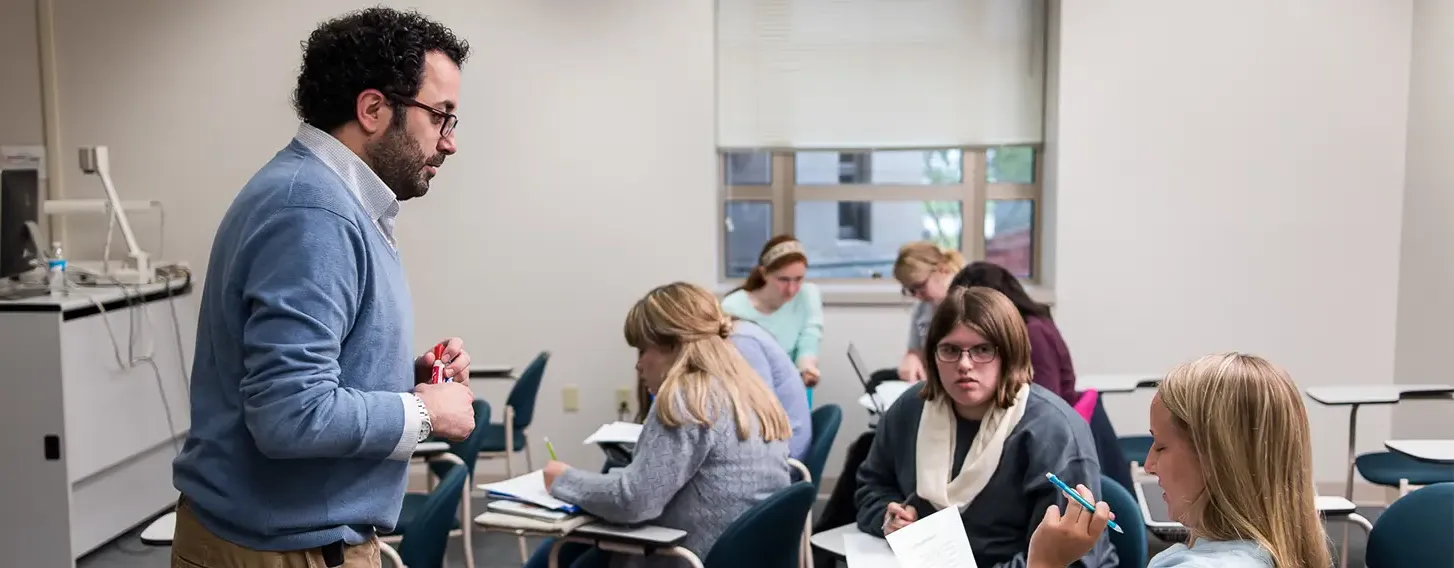 A man standing in front of a classroom full of students, giving a lecture.